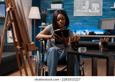 African american female art student wheelchair user taking remote art classes with tablet in home crafts studio. Young drawing schoolgirl using digital tablet to learn new sketching techniques. - Powered by Shutterstock