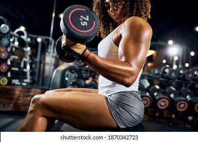 African American female athlete with a pair of dumbbells in her hands performing the seated bicep curl