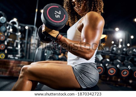 African American female athlete with a pair of dumbbells in her hands performing the seated bicep curl