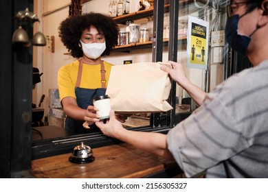 African American Female Barista With Face Mask Works In The Cafe With Social Distance, Takeaway Coffee For A Customer, New Normal Service Of Small Business Coffee Shop In COVID19 Quarantine Lifestyle.