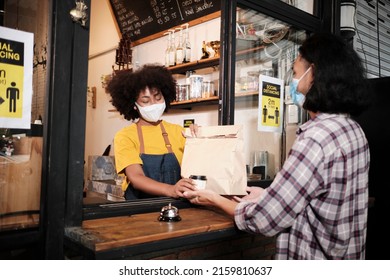 African American Female Barista With Face Mask Works In The Cafe With Social Distance, Takeaway Coffee For A Customer, New Normal Service Of Small Business Coffee Shop In COVID19 Quarantine Lifestyle.