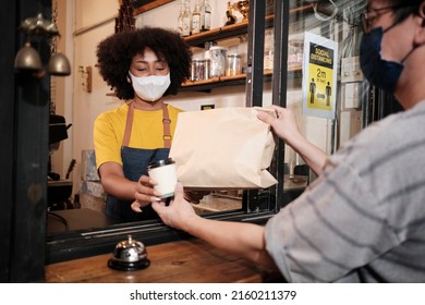 African American Female Barista With Face Mask Works In The Cafe With Social Distance, Takeaway Coffee For A Customer, New Normal Service Of Small Business Coffee Shop In COVID19 Quarantine Lifestyle.