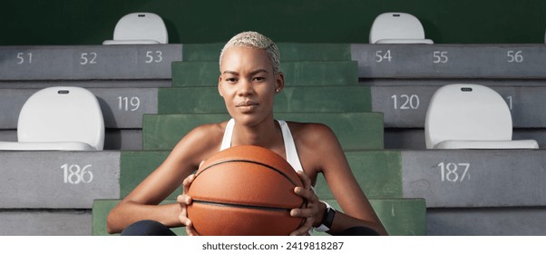 An African American female basket player sitting on the stadium stands, woman holding a basketball, embodying the concept of passion for the sport, game and physical training - Powered by Shutterstock