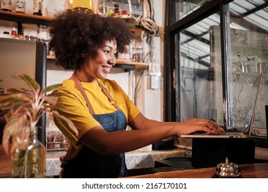 African American Female Cafe Barista In Casual Apron Happy With Online Customer Order In Laptop, Cheerful Works With Smile At Counter Bar In Coffee Shop, Small Business Startup Entrepreneur Lifestyle.