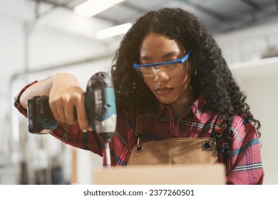 African American female carpenter working with uses hand drill to assemble to timber at wood factory. Female joiner using uses hand drill in wood factory - Powered by Shutterstock