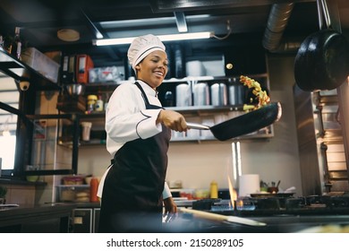 African American female chef having fun while preparing food in the kitchen at restaurant. - Shutterstock ID 2150289105