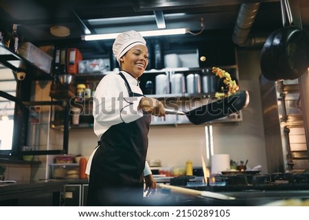 African American female chef having fun while preparing food in the kitchen at restaurant.