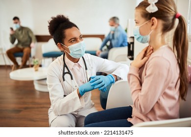 African American female doctor communicating with little girl who is complaining of a sore throat during coronavirus pandemic.  - Shutterstock ID 2214131475