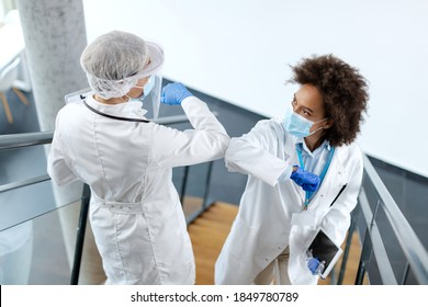 African American female doctor and her colleague elbow bumping while wearing protective face masks at medical clinic.  - Powered by Shutterstock