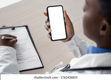 African american female doctor holding using cell phone app mock up white screen, over shoulder closeup view. Healthcare telemedicine online remote consultation mobile medical tech application concept