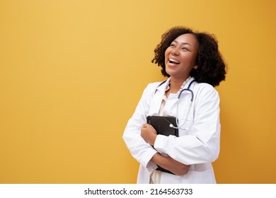 African American Female Doctor Holding Tablet Yellow Background. Smiling Mature Woman Doctor In White Lab Coat Standing Isolate. Successful Happy Healthcare Worker Looking At Camera, Copy Space.