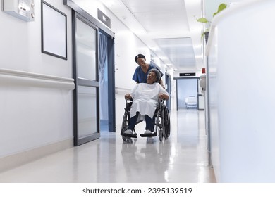 African american female doctor walking with senior female patient in wheelchair in hospital corridor. Medicine, healthcare and medical services, unaltered. - Powered by Shutterstock