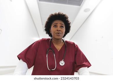 African american female doctor wearing scrubs, running through corridor at hospital. Hospital, medicine, healthcare and work, unaltered. - Powered by Shutterstock