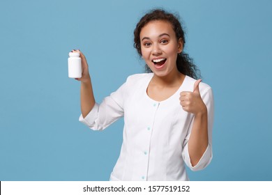 African american female doctor woman in medical gown showing thumb up, holding tablets, aspirin pills in bottle isolated on blue background. Healthcare personnel medicine concept. Mock up copy space