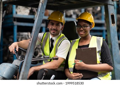 African American Female Employee Worker And Hispanic Man Manager Wearing Safety Hardhat Helmet Working Together On Forklift Truck At Old Auto And Car Parts Warehouse Store.