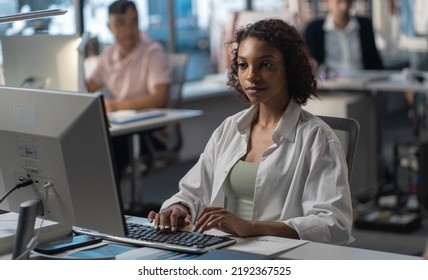 African American Female Employee Working At Her Desk In The Office Located In A Skyscraper. Modern Friendly Working Environment