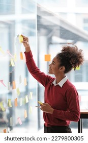 African American female employee write down on colorful sticky notes manage list, concentrated biracial woman work on startup brainstorm collaborate plan on stickers on glass wall - Shutterstock ID 2279800305