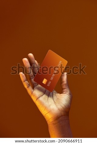 African american female hand holds levitating template Bank credit card with online service on golden orange background