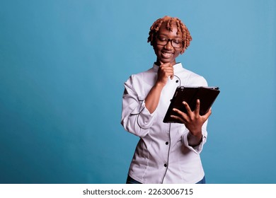 African American female kitchen worker watching recipe videos on tablet screen. Afro chef smiling during work video lesson on electronic device. Woman cook having fun with technology. - Powered by Shutterstock