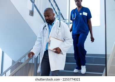 African american female and male doctor walking down hospital staircase. Hospital, medical and healthcare services. - Powered by Shutterstock