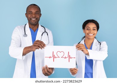 African american female and male doctors holding paper with drawing heart rate, standing over blue studio background and smiling at camera - Powered by Shutterstock