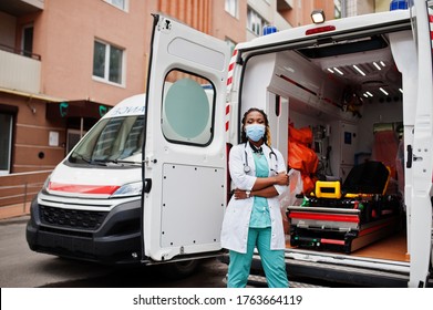 African American Female Paramedic In Face Protective Medical Mask Standing In Front Of Ambulance Car.