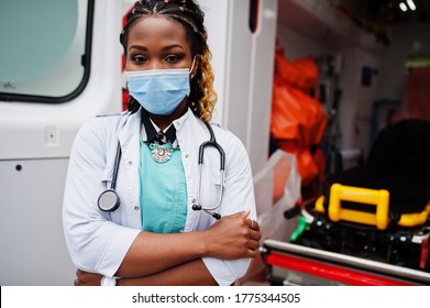 African american female paramedic in face protective medical mask standing in front of ambulance car.
