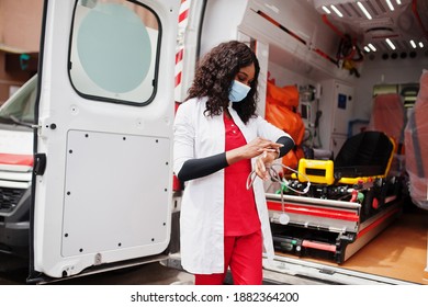 African American Female Paramedic In Face Protective Medical Mask Standing In Front Of Ambulance Car.