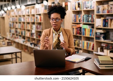 African American Female Professor Using Laptop While Teaching Via Video Call From University Library.