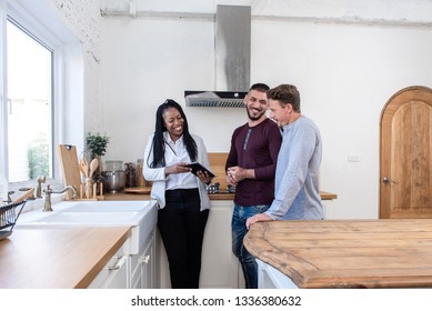 African American Female Real Estate Agent In Kitchen Showing Gay Couple Around New House