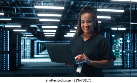 African American Female IT Specialist Using Laptop Computer, Standing in Big Warehouse Data Center. System Administrator working with SAAS, Cloud Web Services. E-Business Digital Entrepreneur - Powered by Shutterstock