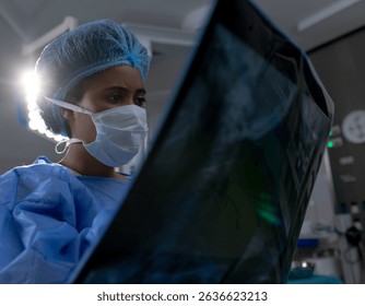 African American female surgeon examining X-ray film against surgical lamp in operating room. Medical, healthcare, diagnostic, clinical, professional, technology, hospital