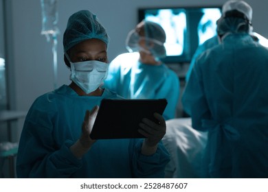 African american female surgeon wearing surgical gown using tablet in operating theatre at hospital. Hospital, communication, surgery, hygiene, medicine, healthcare and work, unaltered. - Powered by Shutterstock