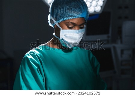 African american female surgeon wearing surgical gown and face mask in operating theatre. Hospital, surgery, medicine, healthcare and work, unaltered.