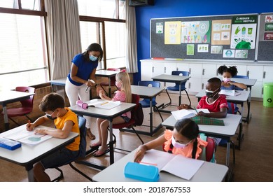 African American Female Teacher Spraying Hand Sanitizer On Hands Of Girl At Elementary School. Education Back To School Health Safety During Covid19 Coronavirus Pandemic