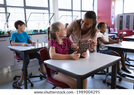 African american female teacher teaching caucasian girl to use digital tablet in the class at school. school and education concept