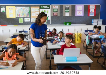 African american female teacher teaching caucasian boy to use digital tablet at elementary school. school and education concept