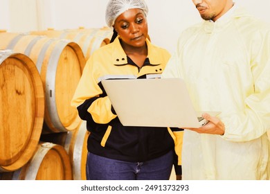 African American female worker consults with an Asian American worker inspect wine fermentation room providing advice inspections temperature oak barrel rooms maintaining quality within the winery. - Powered by Shutterstock