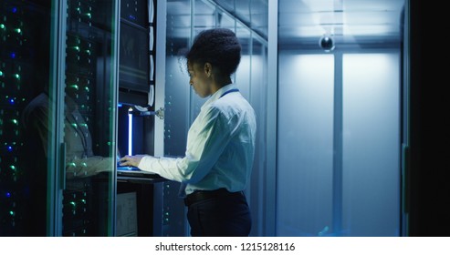 African American Female IT Worker Diagnosing Server Hardware In Modern Data Server With Rows Of Server Racks