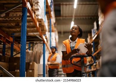 African American female worker going through inventory list while checking stock at distribution warehouse. - Shutterstock ID 2154986023