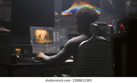 African American film editor does color grading on computer in modern studio. Big monitors with RGB colour correction graphic bar and program interface on the wall. Video post production. Handheld. - Shutterstock ID 2288812383