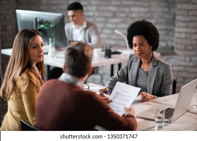 African American Financial Advisor Going Through Paperwork With Her Clients While Having A Meeting In The Office.