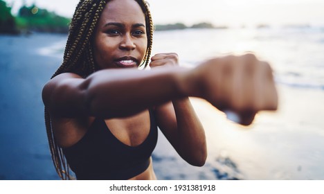 African American fit girl in tracksuit practice power punches on seashore, concentrated sportswoman training and boxing during workout process, concept of healthy lifestyle and motivation for goal