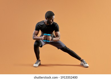 african american fitness sportsman is doing exercise squatting with dumbbells, isolated on brown studio background - Powered by Shutterstock