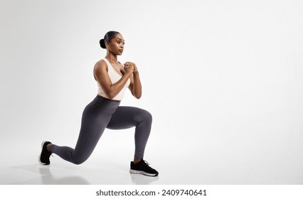 African American fitness woman stretching legs performing forward lunges over white studio backdrop, enjoying workout routine, looking aside. Full length shot, empty space - Powered by Shutterstock