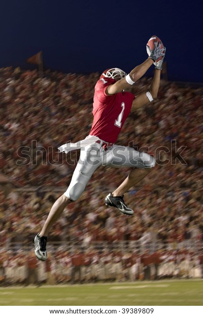 African American football wide
receiver leaping up to catch a football. Vertically framed
shot.