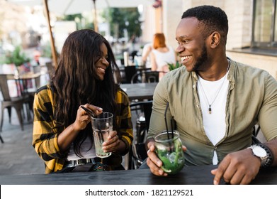 African American Friends, Young Man And Woman Are Sitting In A Cafe Drinking Refreshing Cocktails And Having Fun Talking