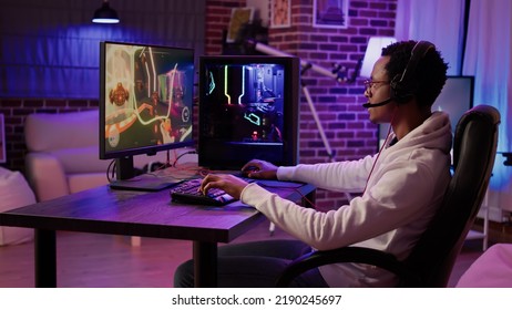 African american gamer playing intense action game in tournament talking with team using gaming headset at home. Man having intense experience streaming online first person shooter game on pc - Shutterstock ID 2190245697