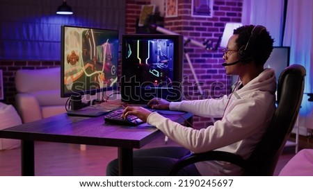 African american gamer playing intense action game in tournament talking with team using gaming headset at home. Man having intense experience streaming online first person shooter game on pc