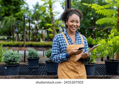 African American gardener nad nursery owner is holding clipboard while working in her conifer tree nursery garden center for evergreen and bonsai artist supply concept - Powered by Shutterstock